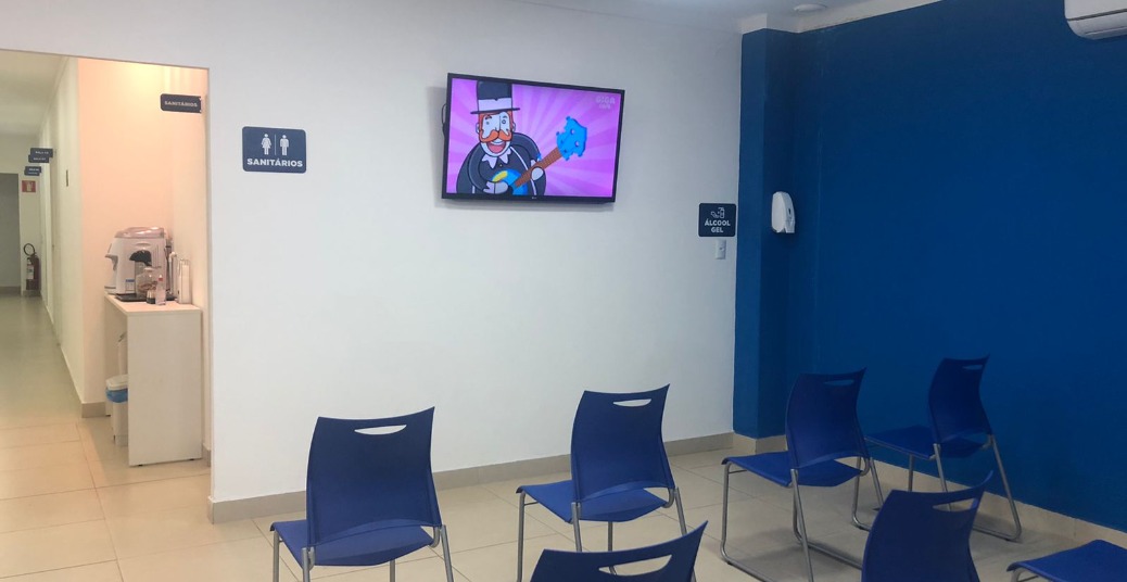 Sala de espera da Eloclin com cadeiras, televisão e acesso ao corredor interno